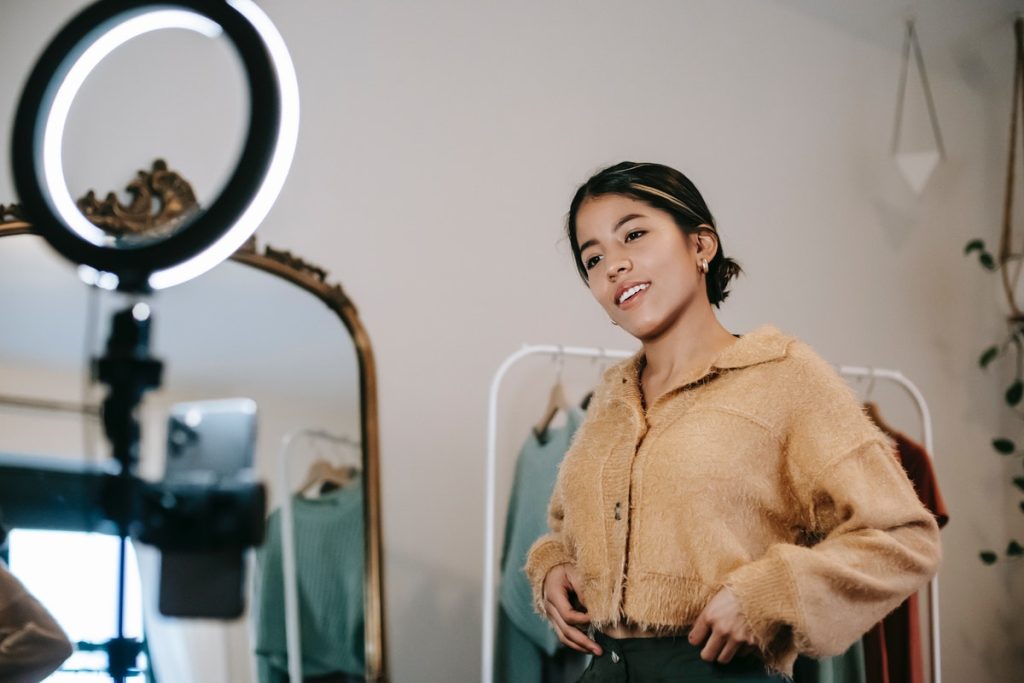 Woman standing in bedroom in front of a ring light filming or photographing influencer content.