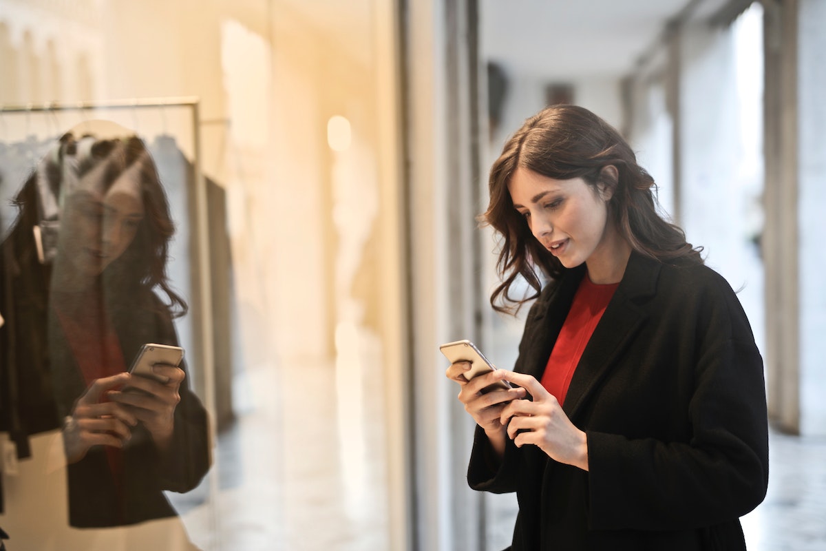 Woman standing in front of a shop window using her phone for social shopping online.