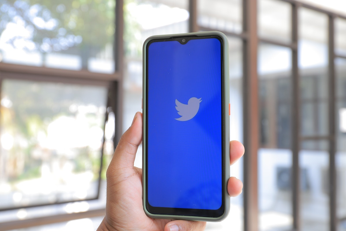Hand holding a phone with the Twitter logo on the screen.
