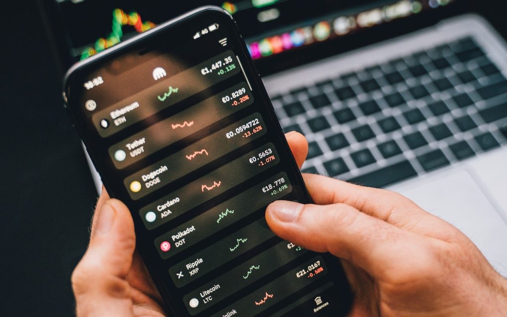 Hands holding a phone with a list of cryptocurrencies and their value.