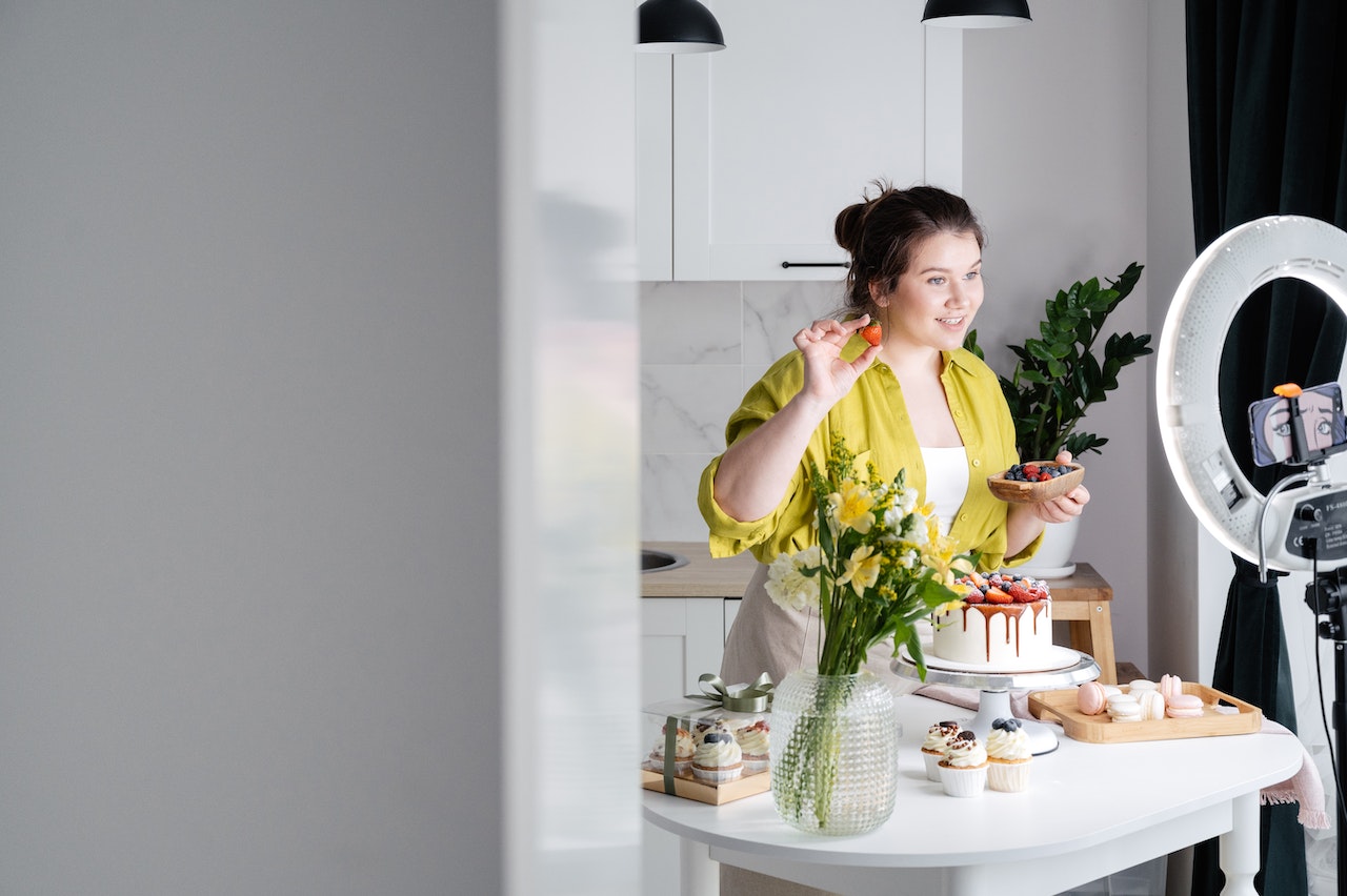 Woman standing in a kitchen behind an island with delicious desserts, creating influencer content about food.