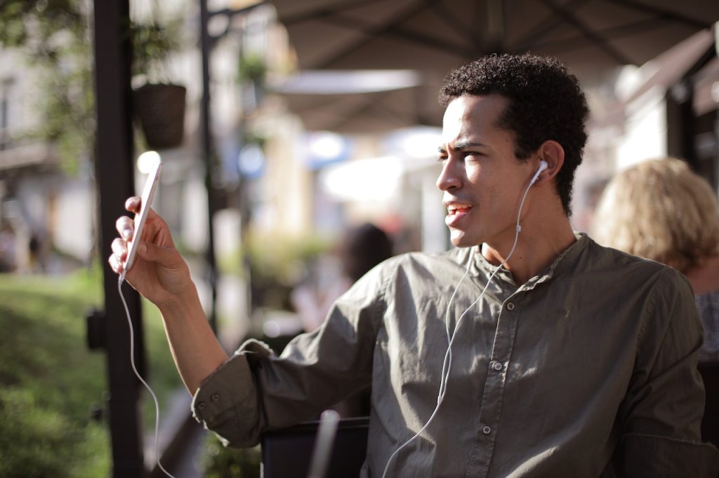 Man wearing ear buds and holding phone up to film a video.