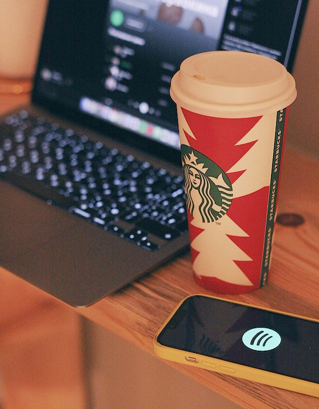 A co-op advertising example image with a desk that has a laptop computer with Spotify showing on the screen, a phone with the Spotify logo and a Starbucks cup.