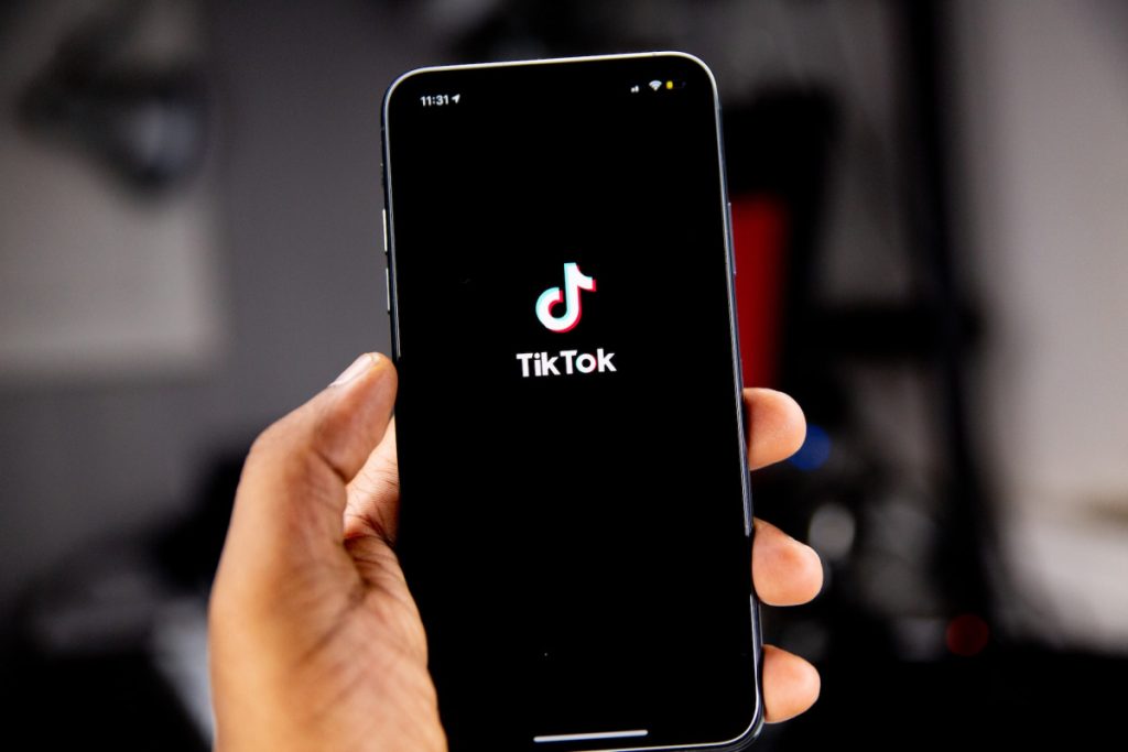 Hand holding up a phone with the TikTok Now app showing on the screen.