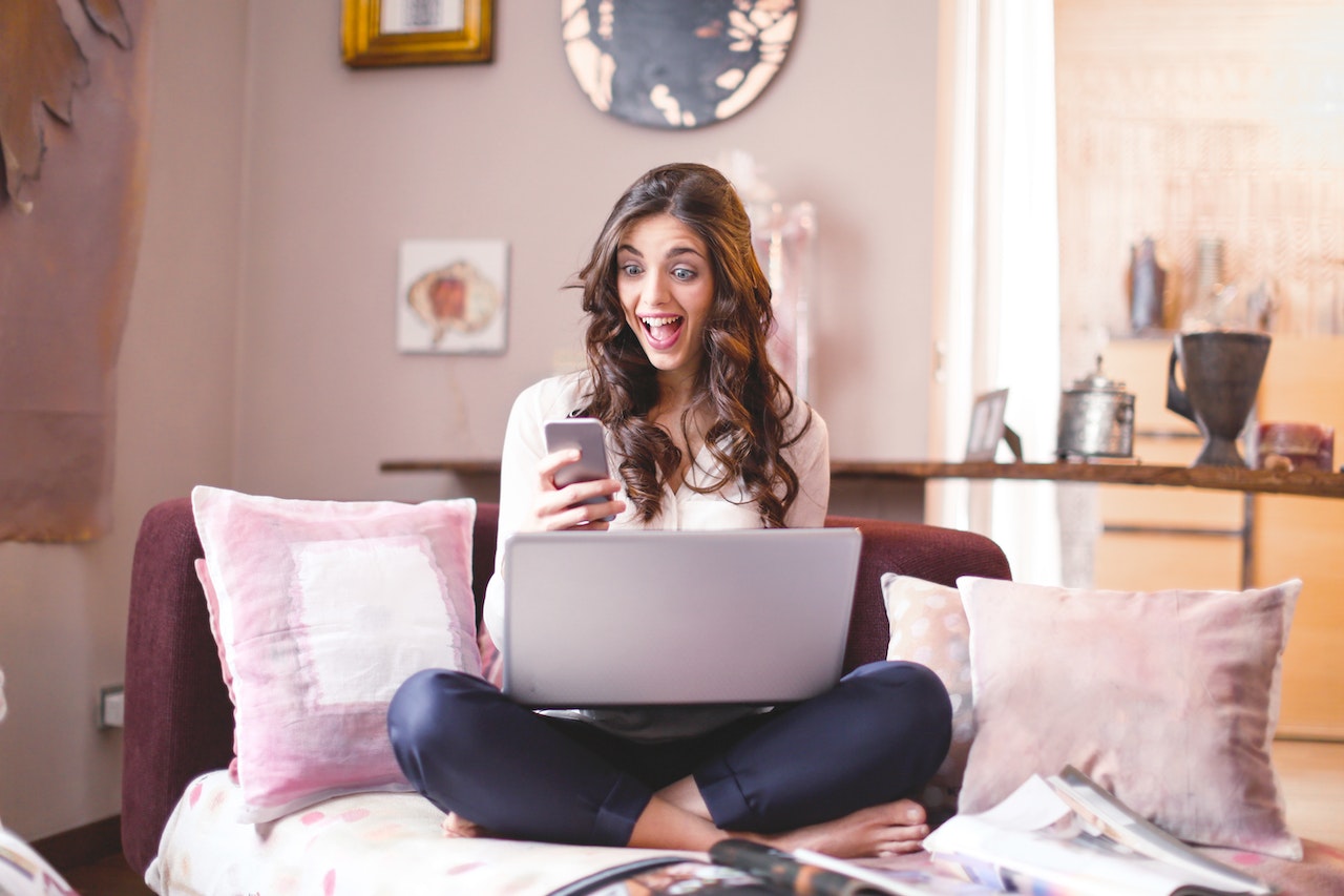 Woman sitting on a couch with a computer and cell phone.