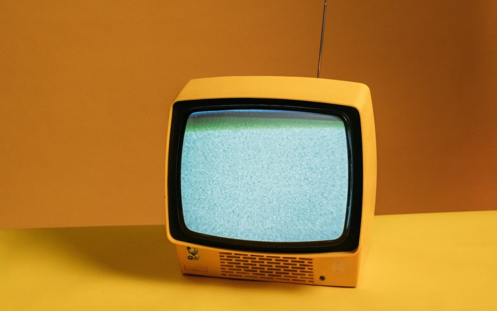 Yellow vintage television sitting on a yellow table with darker yellow background.