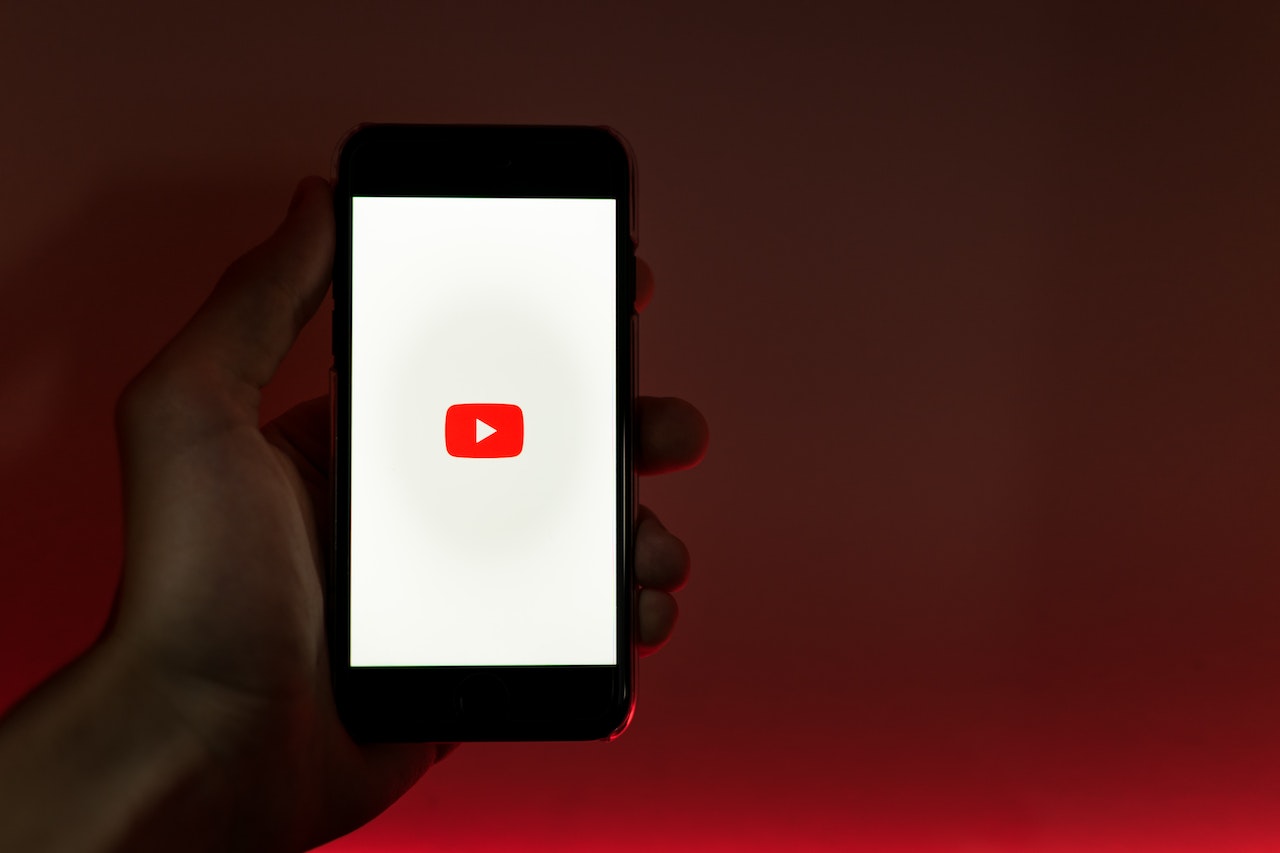 Hand holding phone with YouTube logo displayed on the screen.