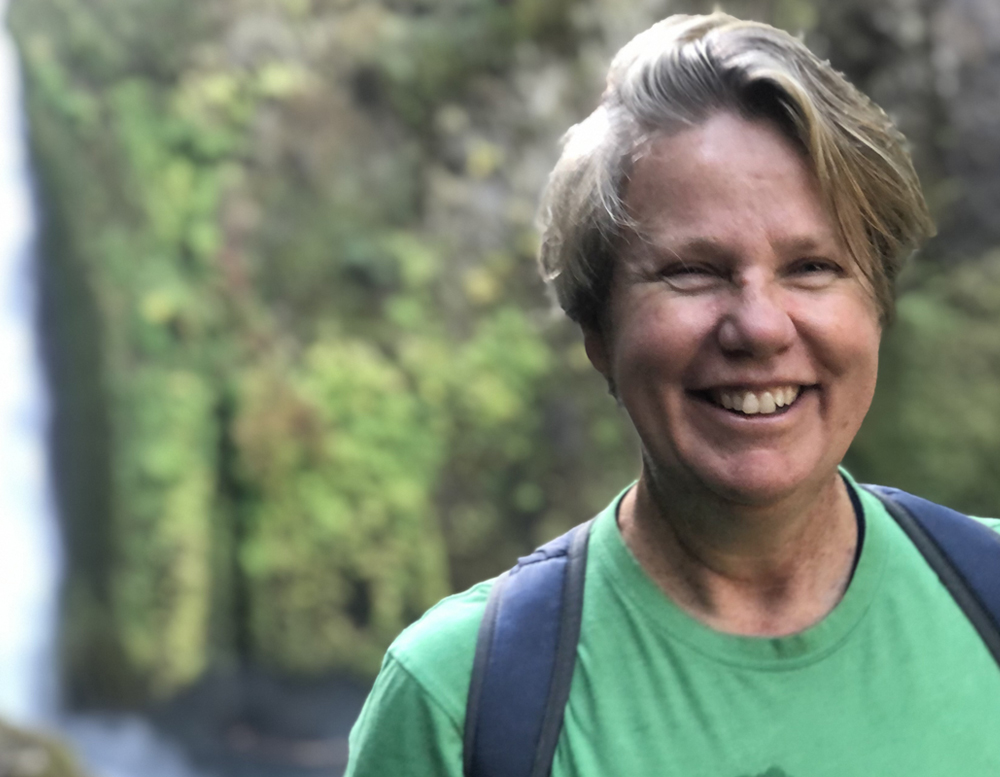 Shoppable content expert, Bridget Fahrland stands smiling in the wilderness with a green t-shirt and backpack