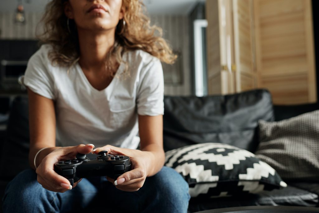 A female gaming influencers sitting on a couch and using a game controller to play a console game.