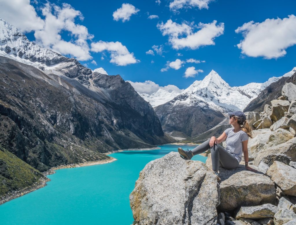 Woman sitting on rocks overlooking a brilliant blue lake and large mountains is a great example of imagery for travel influencer marketing campaigns.