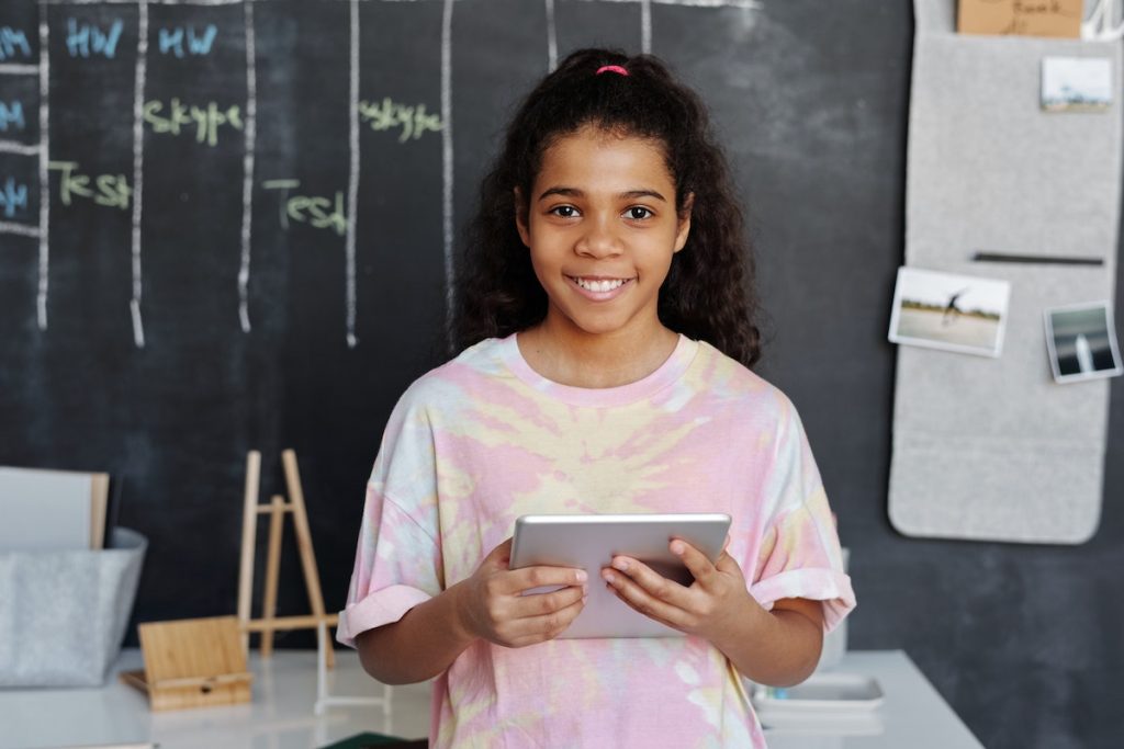 Girl from the Gen Alpha generation standing in front of a desk holding a tablet.