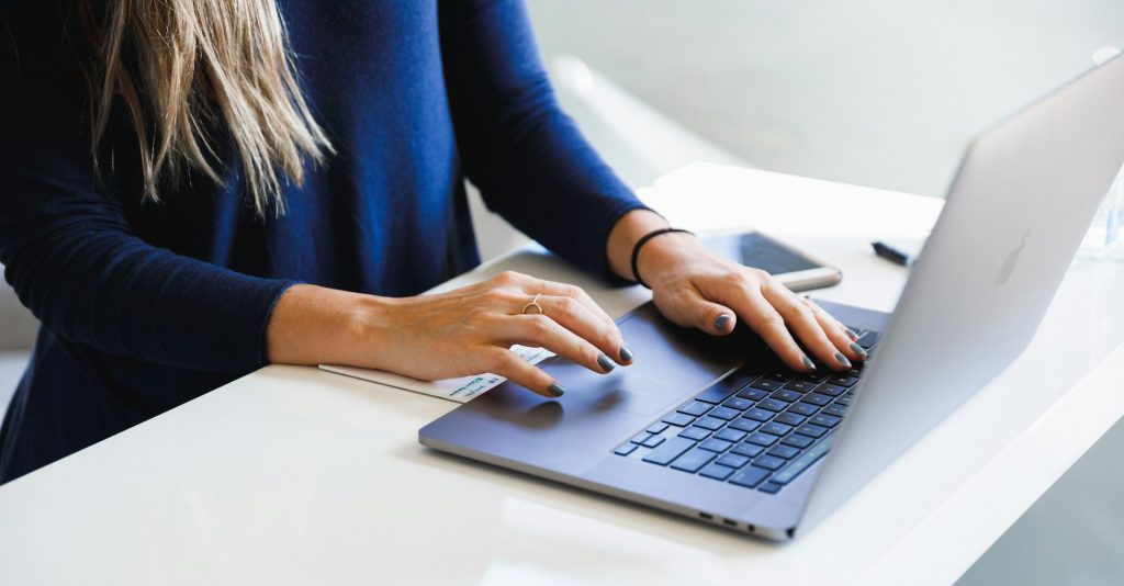 A woman in a blue shirt sitting at her desk viewing long form content on her laptop.