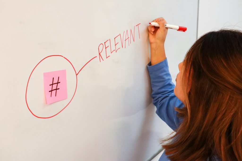 Woman writing on a white board with a sticky note that has a hashtag on it.