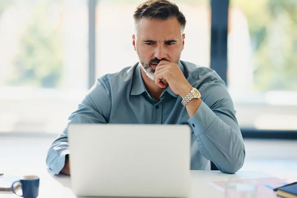 Man sitting at desk in front of computer, looking perplexed.