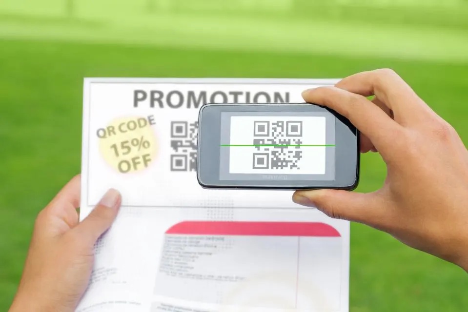 A hand is seen pointing a cell phone at a piece of paper to scan a QR code.