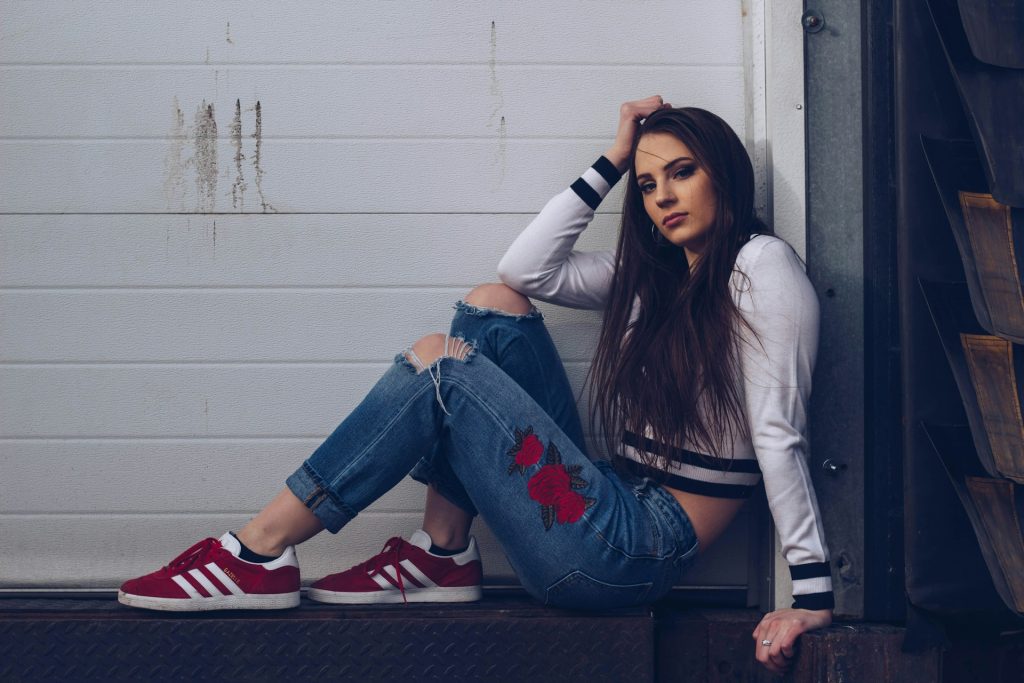 In an example of niche influencer marketing, a young woman sits by a wall with embroidered jeans.