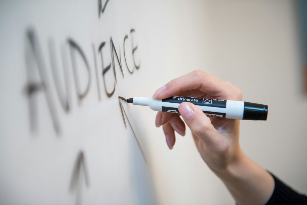 Hand writing the word audience on a white board.