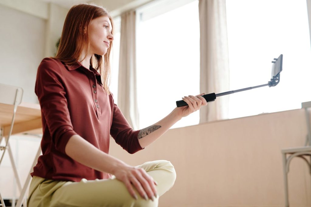 Influencer sitting on the floor holding a selfie stick with a phone, filming creative.