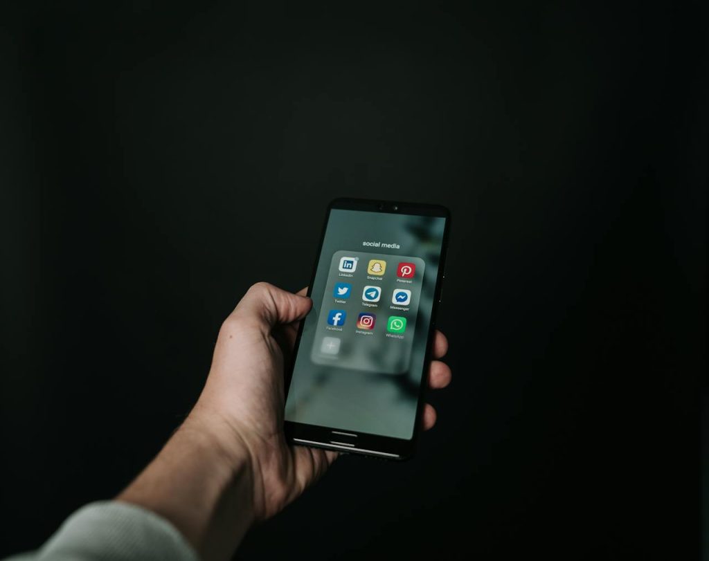 Hand holding cell phone against a black background with a folder showing major social media app icons that are often used for influencer marketing.