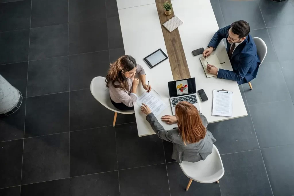 Three people sitting at the end of a long table working, as viewed from above.